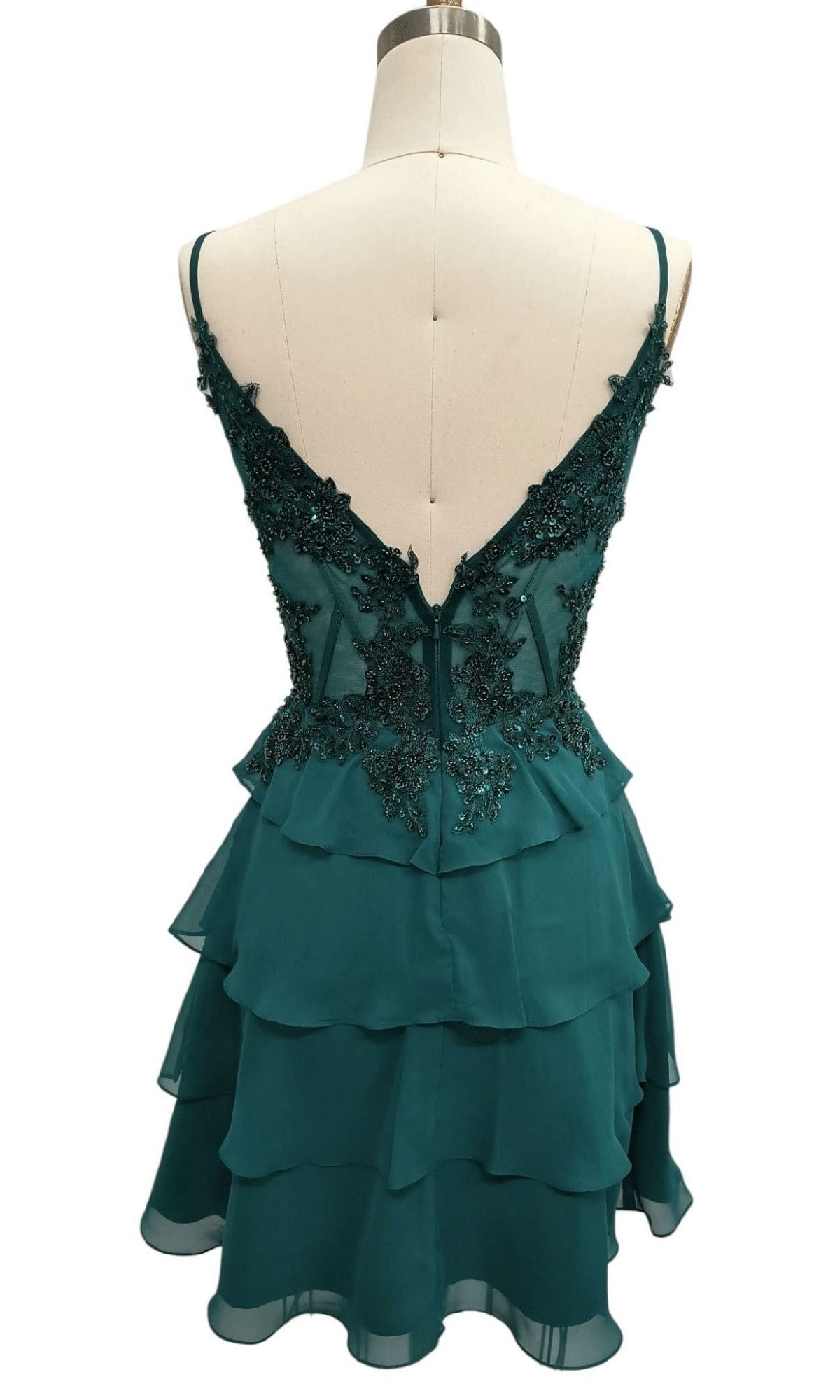 The Tiered Emerald Green Hoco Dress by Dave & Johnny features a sleeveless bodice, tiered ruffle skirt, deep V-back, and black beaded appliques, displayed on a mannequin.